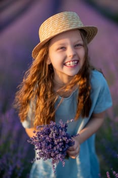 Lavender sunset girl. A laughing girl in a blue dress with flowing hair in a hat walks through a lilac field, holds a bouquet of lavender in her hands