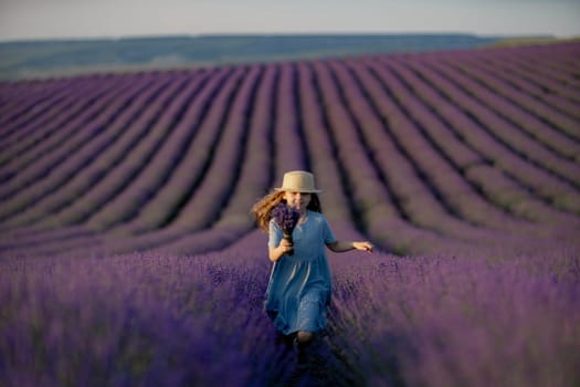 Lavender sunset girl. A girl in a blue dress with flowing hair in a hat runs through a lilac field of lavender. Aromatherapy travel