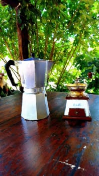 A moka coffee maker and an antique coffee grinder on the table in the garden on a summer morning.