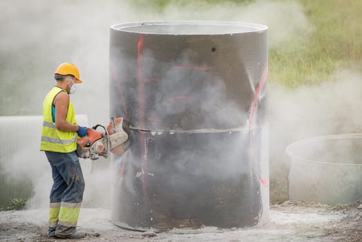 Reconstruction of the road in the city. A worker cuts holes in a concrete barrel to collect rainwater installed under the pavement. Use of a helmet and respirator, compliance with safety regulations