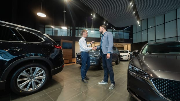 Caucasian man shakes hands with a salesman in a car dealership. Car purchase deal