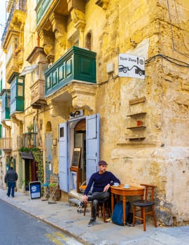 Men drinking coffee on a terrace outside at the Colorful Streets of Valletta Malta, a City trip at the capital of Malta with Streets full of color balconies.