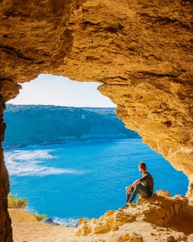 Gozo Island Malta, a young man and a View of Ramla Bay, from inside Tal Mixta Cave Gozo looking out over the blue ocean on a bright day during winter in Malta