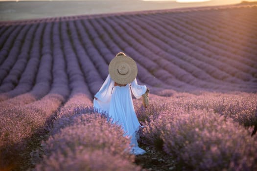 Happy woman in a white dress and straw hat strolling through a lavender field at sunrise, taking in the tranquil atmosphere