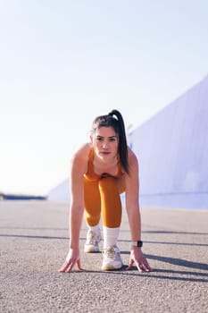 vertical photo of a concentrated sportswoman in position to start a race in a sunny day, concept of sport and active lifestyle, copy space for text