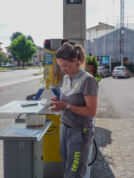 Cremona, Italy - July 3 2023 gas station attendant woman taking payments with credit card from customers outdoors near fuel pumps