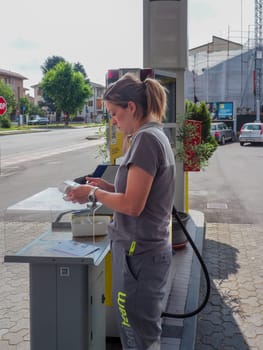 Cremona, Italy - July 3 2023 gas station attendant woman taking payments with credit card from customers outdoors near fuel pumps