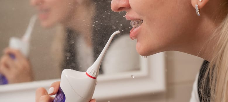 A woman with braces on her teeth uses an irrigator. Close-up portrait