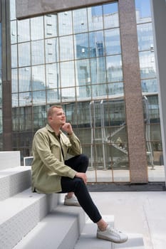 Thoughtful caucasian guy with a hearing aid sits on the stairs in the city center