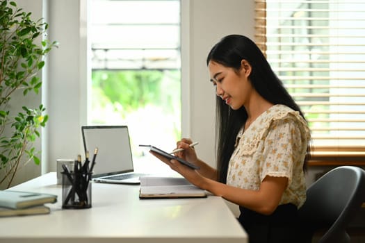 Young Asian woman using digital tablet, browsing internet, remote work, stying online at home..