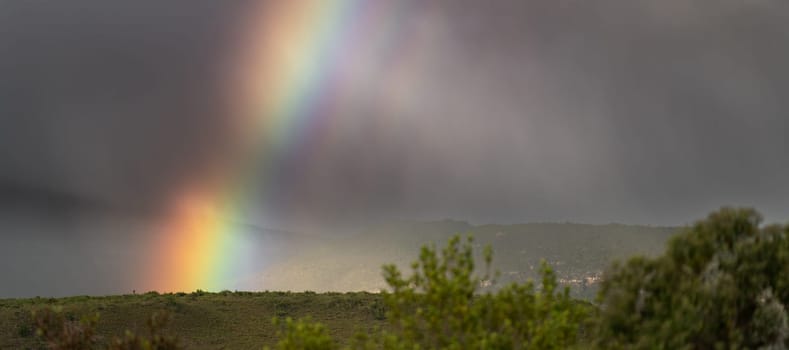 A bright rainbow spans a grassy plain under a darkening pre-storm sky, providing ample space for text.