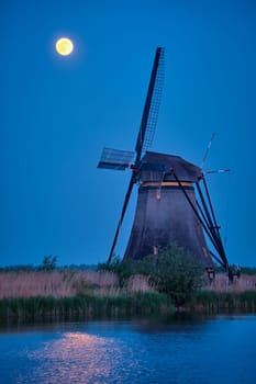 Netherlands rural lanscape with windmills at famous tourist site Kinderdijk in Holland in twilight with full moon