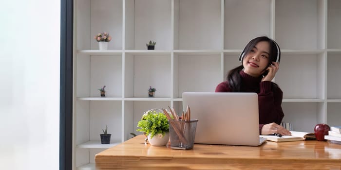 Asia women wear wireless headphone study online write notes look at laptop in living room, distant education.