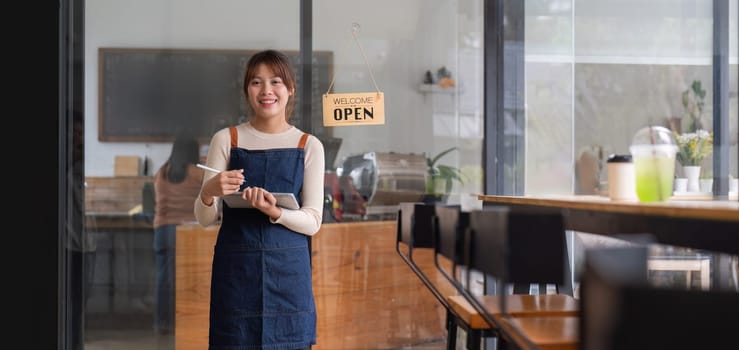 Asian woman barista holding tablet for checking order from customer on blurred coffee cafe shop background , SME business concept.