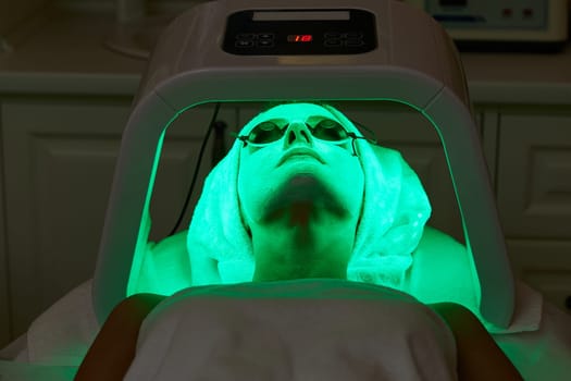 Woman in protective glasses getting facial treatment with led therapy. LED mask at the beauty clinic