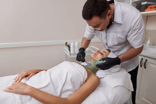 beautician applies green alginate mask to the face of beautiful woman in the spa salon. spa treatments