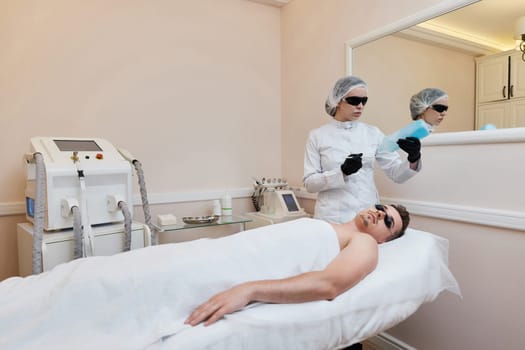 beautician applies cooling gel to male facefor receiving epilation in beauty center.