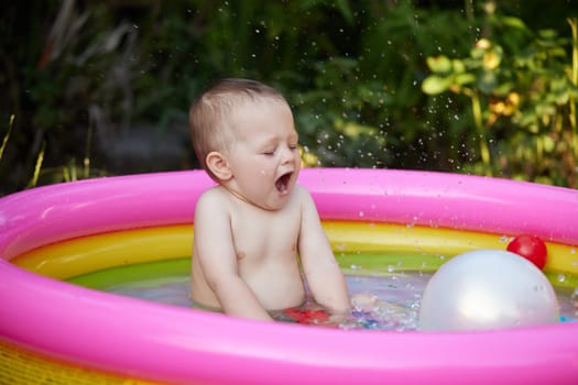 Happy cute baby girl with ball in kid inflatable pool in the garden