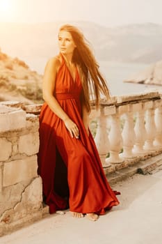 Woman red dress. Summer lifestyle of a happy woman posing near a fence with balusters over the sea