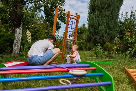 Dad with little child girl daughter collects wooden home sports complex outdoor. assembly process