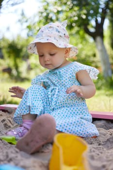 cute little girl playing in sand in sandbox with various toys on outdoor playground on sunny summer day.