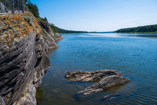 Beautiful, wide autumn river among forests and rocky shore. A calm and quiet place with autumn colors. Reflection of clouds in the water in good weather