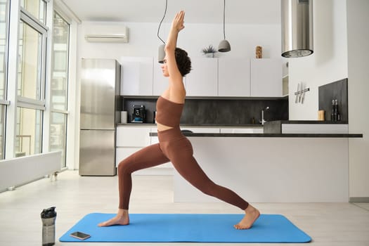 Yoga concept. Sporty woman stretching on mat over light windows, doing asana, midnful training.