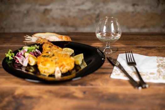 monkfish au gratin plate with composition on wooden top and wine glass and cutlery
