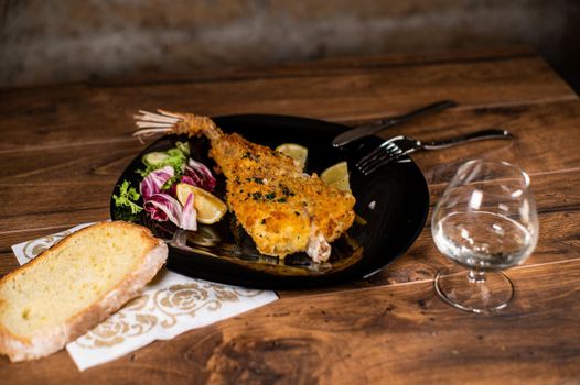 monkfish au gratin plate with composition on wooden top and wine glass and cutlery