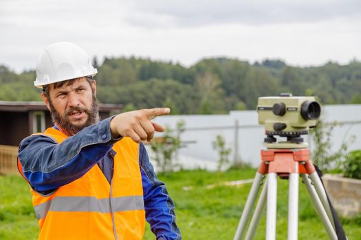 A civil engineer with an optical level waves his hand to control colleagues from a distance. A bearded man leads his subordinates.