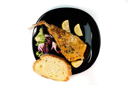 black plate with breaded monkfish on white background