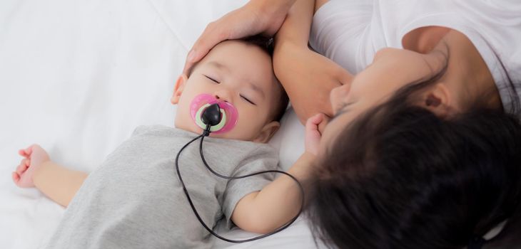 Young asian mother touch head of little baby girl with tender on bed in the bedroom, mom love newborn and care, woman with expression with child together, parent and daughter, family concept.