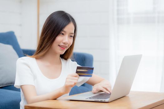 Young asian woman sit on sofa using laptop computer shopping online with credit card buying to internet, happy girl payment with e-business on couch, purchase and payment, business concept.