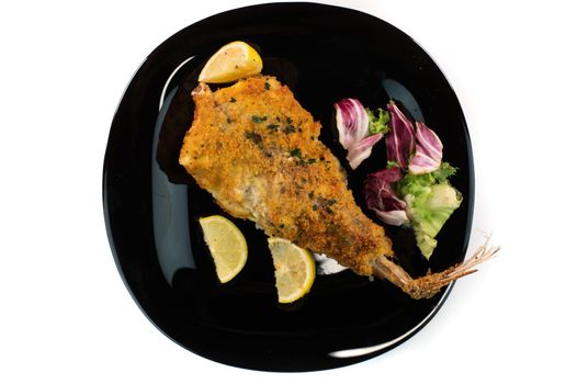 black plate with breaded monkfish on white background