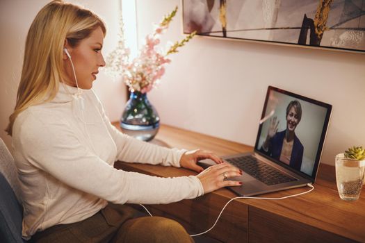 Shot of a young business woman working online from home. She is using her laptop and having video conference at cozy atmosphere during pandemic Covid-19 virus.