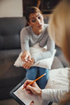 Shot of a stressed out young woman having a discussion with her female psychotherapist while being seated on a sofa inside of a living room.