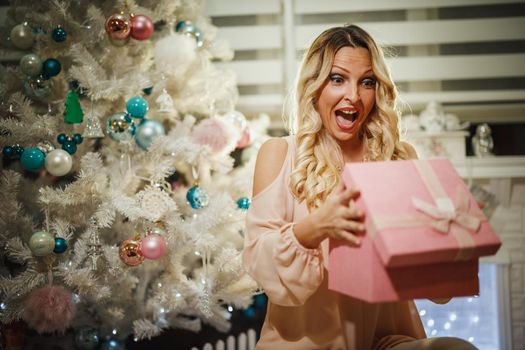 Shot of an attractive young woman opening her Christmas gift by a white Christmas tree at the home.