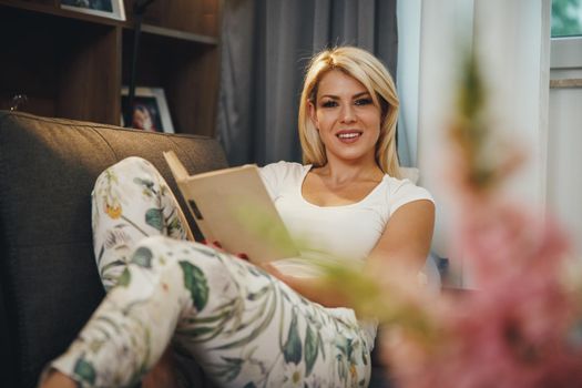 Shot of a beautiful young woman lying on the living room on the sofa, reading a book and relaxing at home.
