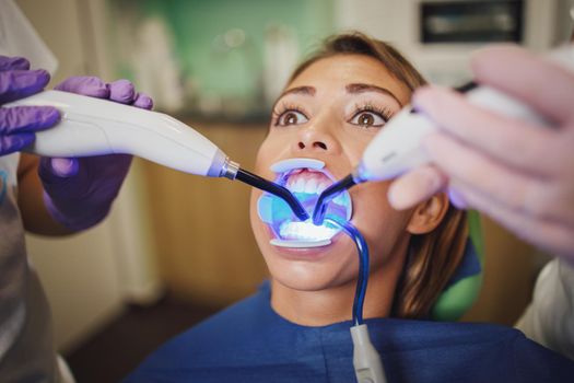 Shot of a beautiful young woman is at the dentist. She sits in the dentist's chair and the dentist fixed lingual locks on her teeth with curing light.