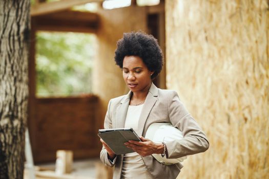 Shot of an African female architect using a digital tablet and checking construction site of a new wooden house.