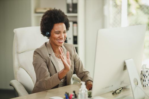 Shot of an African businesswoman wearing a headset and waving hello while working at her desk during corona virus pandemic.