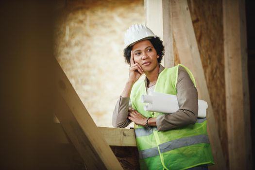 Shot of an African female architect checking construction site of a new wooden house. She is wearing protective workwear and white helmet.