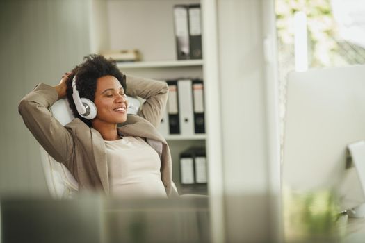 Shot of an African woman relaxing and listening music on the headphones while working on computer in her home office.