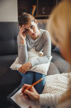 Shot of a worried young woman having a discussion with her female psychotherapist while being seated on a sofa inside of a living room.