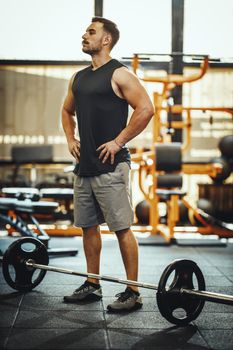 Shot of a muscular guy in sportswear working out with barbell at the cross training gym. 