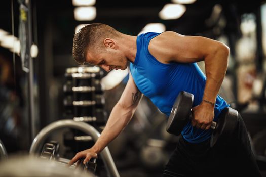 Shot of a muscular guy in sportswear working out at the hard training in the gym. He is pumping up back muscule with heavy weight.