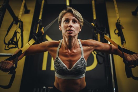 Shot of an muscular mature woman working out with trx straps at the gym.
