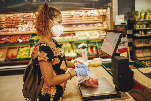 Shot of a young woman is wearing N95 protective mask while buying groceries in supermarket during Covid-19 pandemic.