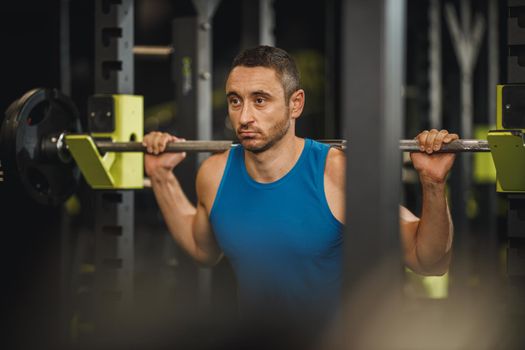 Shot of a muscular guy in sportswear working out at the cross training gym. He is doing squat exercises with barbell.