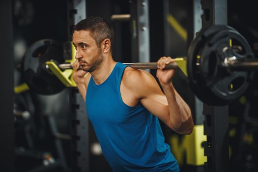 Shot of a muscular guy in sportswear working out at the cross training gym. He is doing squat exercises with barbell.
